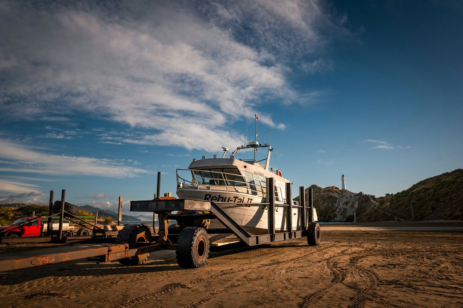 Boat on a transport trailer at sunrise near a coastal lighthouse